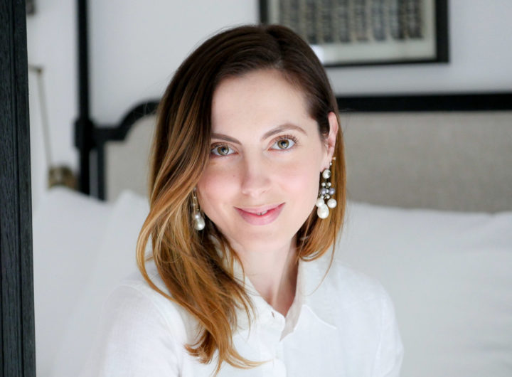 Eva Amurri Martino sits on her bed wearing a white shirt dress, in an "after" pic from using SKII Facial Treatment Essence