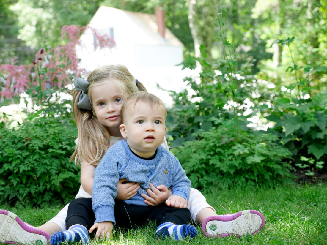 Two year old Marlowe Martino embraces 9 month old brother Major on the grass in Bar Harbor, Maine