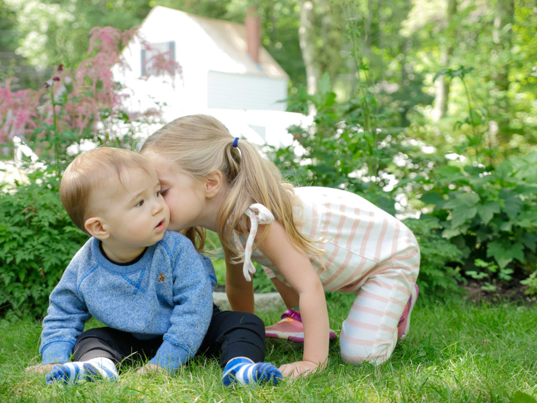 Marlowe Martino leans in to kiss her baby brother Major on the grass in Bar Harbor Maine