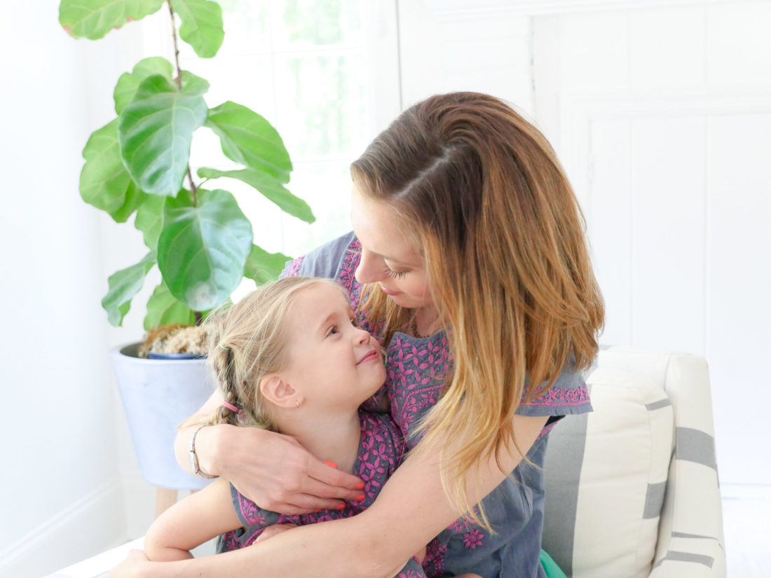 Eva Amurri Martino and Marlowe Martino wear matching embroidered dresses and sit together in a striped armchair in the family room of their Connecticut home