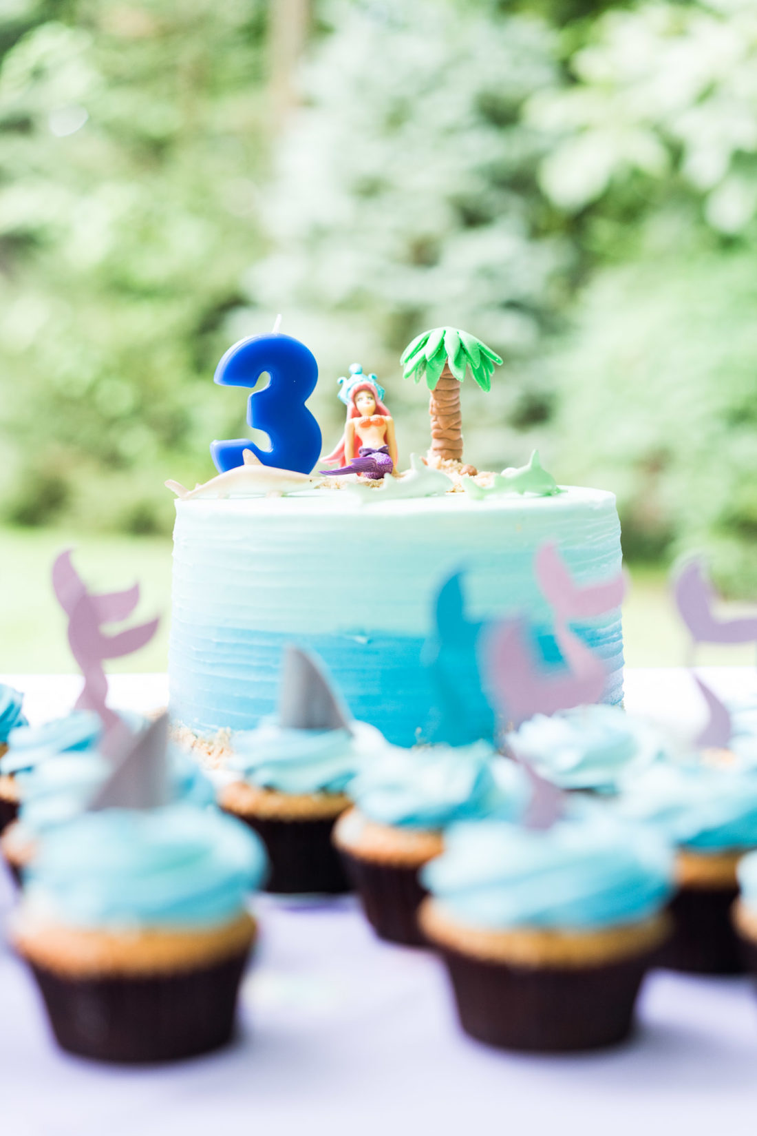 Marlowe Martino's Mermaid and Shark themed birthday cake sits on a table surrounded by cupcakes