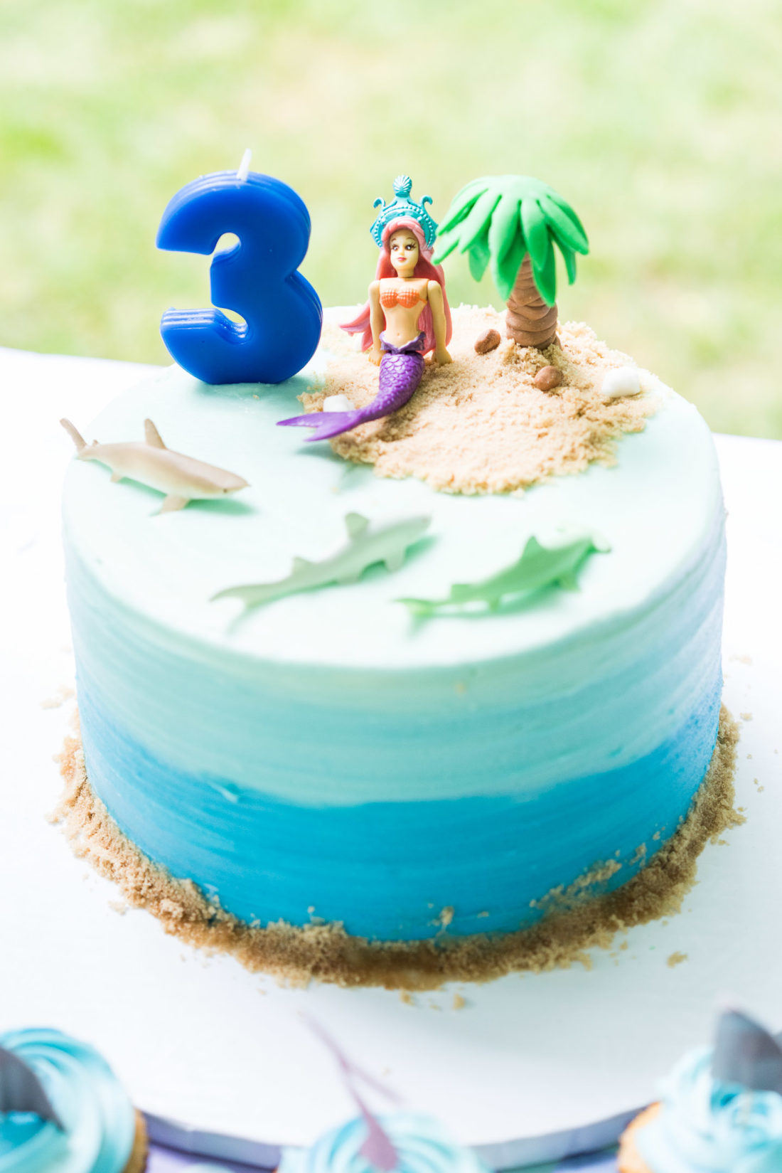 Marlowe Martino's Mermaid and Shark themed birthday cake sits on a table surrounded by cupcakes