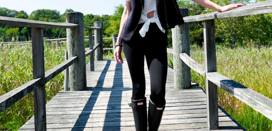 Eva Amurri Martino wears black Hunter wellington rain boots and black leggings as she stands on a bridge in Connecticut