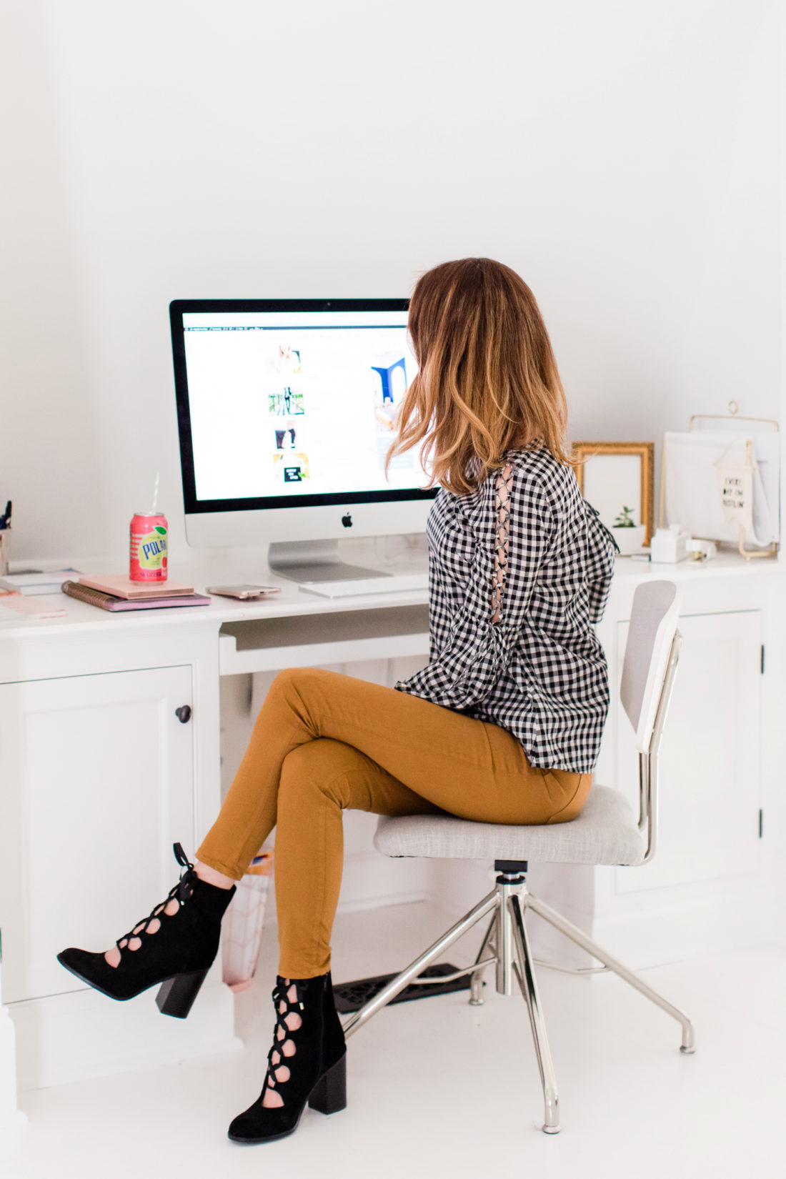 Eva Amurri Martino wears tan jeans and a black and white checked top, and sits at her computer in the Happily Eva After studio