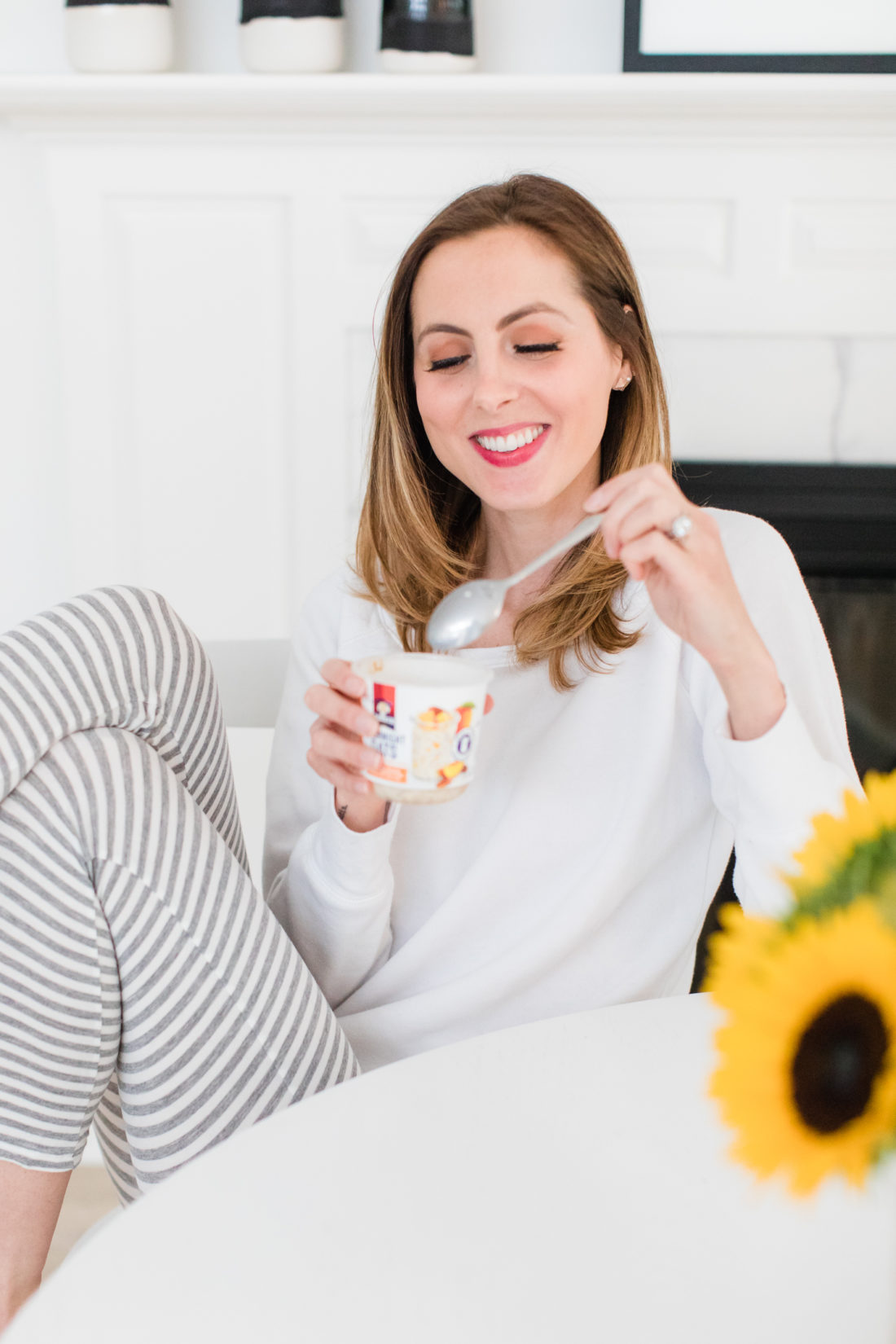 Eva Amurri Martino sits at the kitchen table in a pair of grey and white striped pajamas and eat breakfast next to a vase of sunflowers
