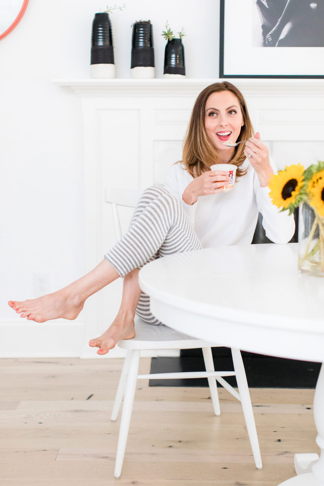 Eva Amurri Martino sits at the kitchen table in a pair of grey and white striped pajamas and eat breakfast next to a vase of sunflowers