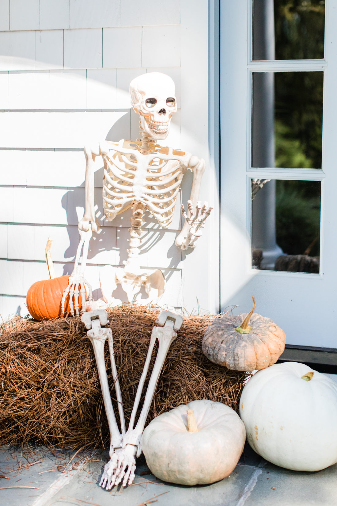 A skeleton sits on a bale of pine needles, surrounded by pumpkins in the spooky entryway of Eva Amurri Martino's Connecticut home