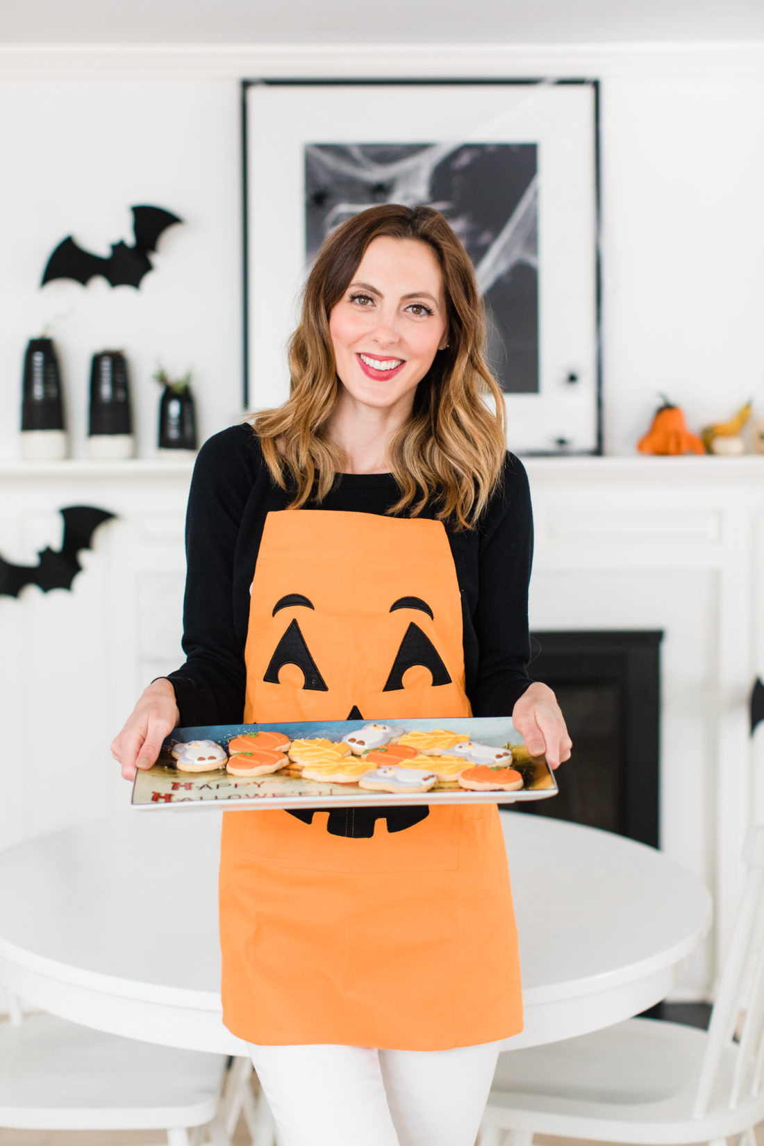 Eva Amurri Martino wears a jack-o-lantern apron and holds a tray of fall-themed cookies for her guests