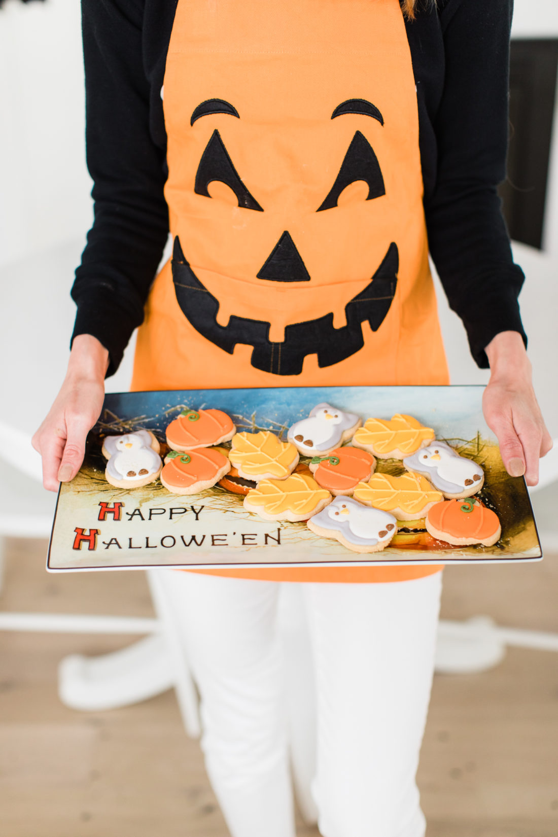 Eva Amurri Martino wears a jack-o-lantern apron and holds a tray of fall-themed cookies for her guests