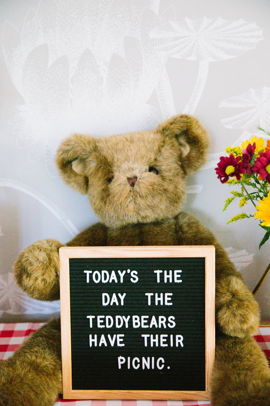 A teddy bear holds a felt board announcing the teddy bear theme of Major Martino's first birthday party