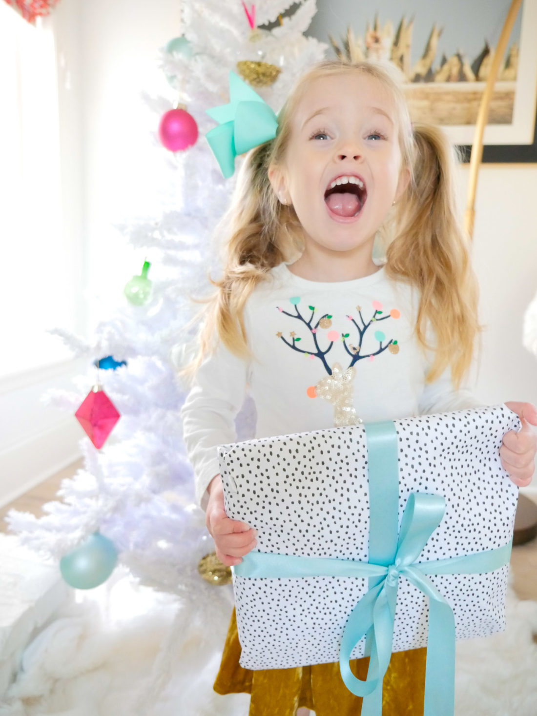 Marlowe Martino shrieks with joy as she holds a colorful christmas present in front of the white and pastel christmas tree in her Connecticut home