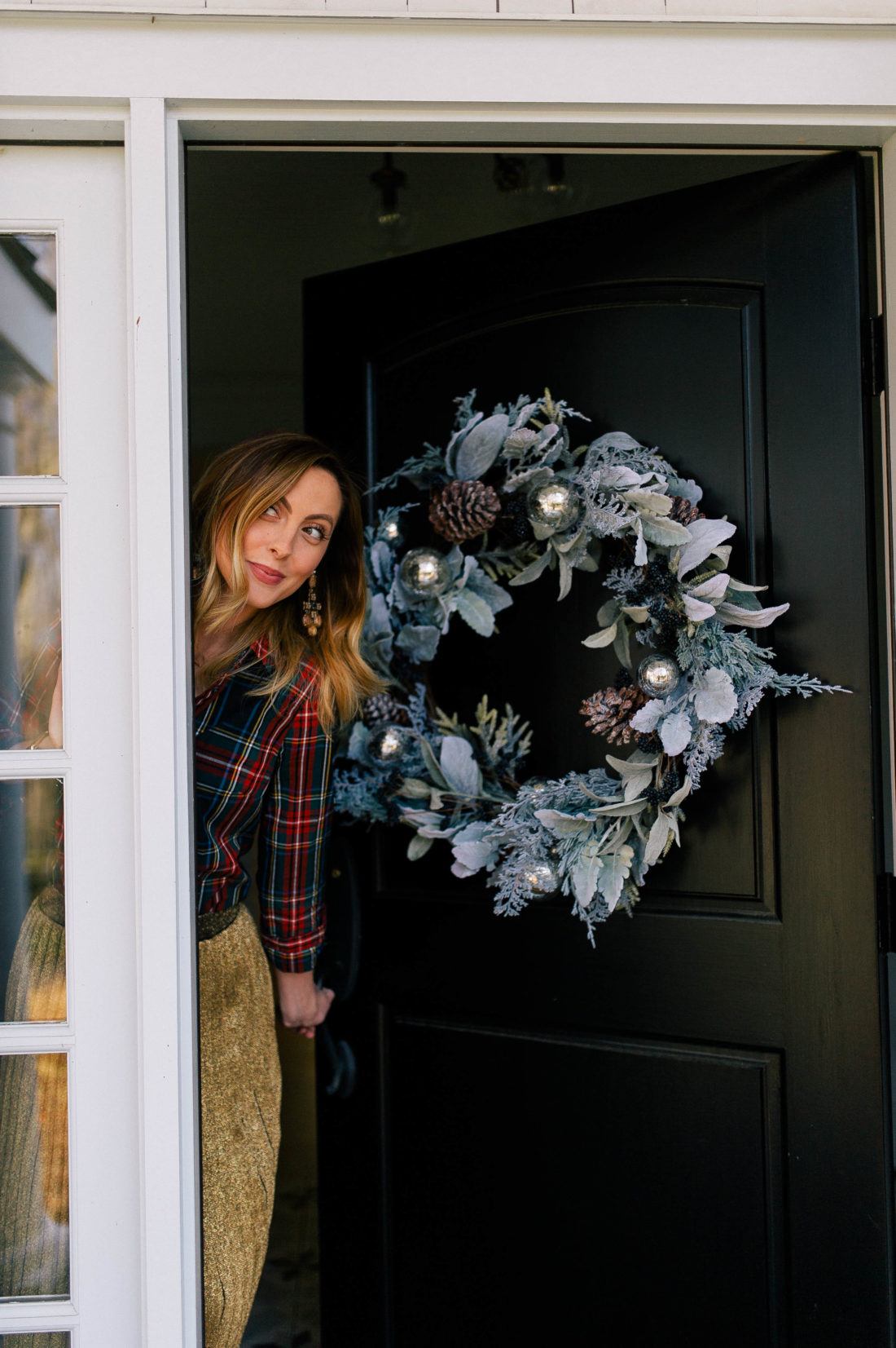 Eva Amurri Martino peeks out behind her front door which is adorned with a blue and sage colored christmas wreath