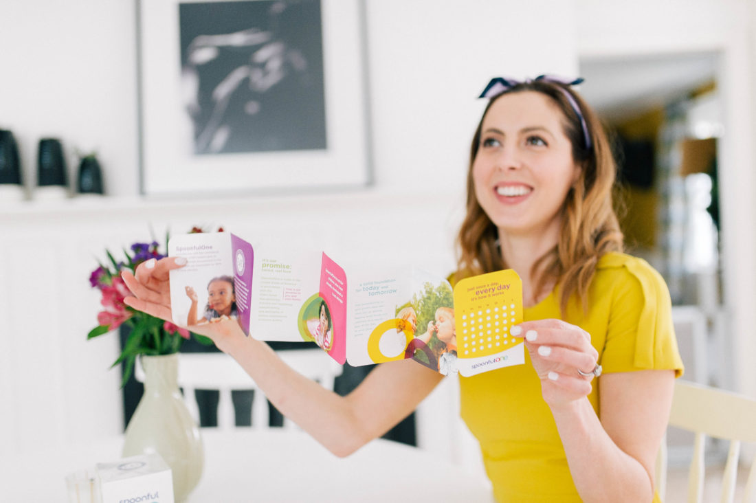 Eva Amurri Martino wears a yellow dress and reads the directions of SpoonfulOne mixins