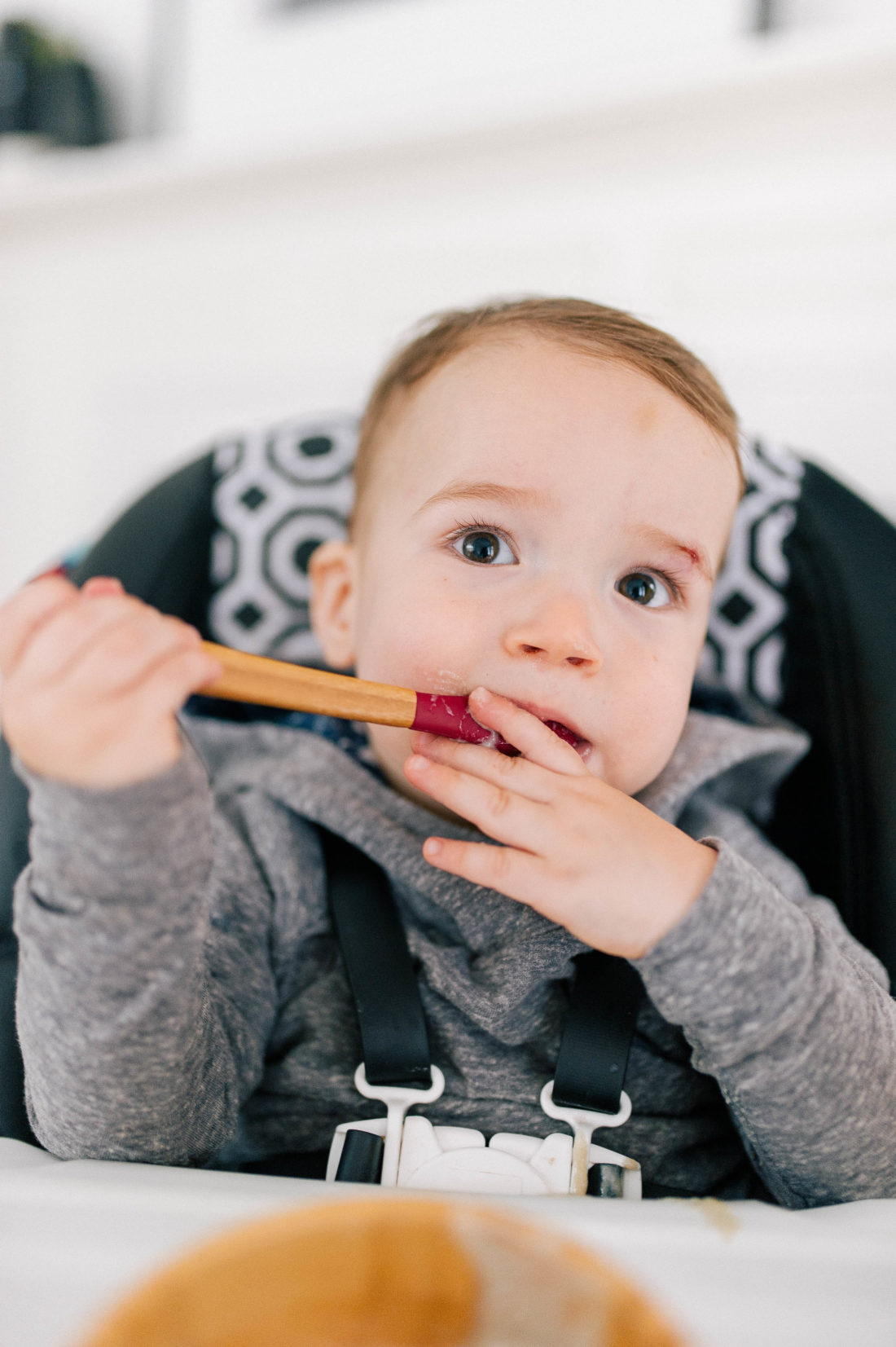 Major Martino feeds himself in his high chair wearing a hoodie sweatshirt