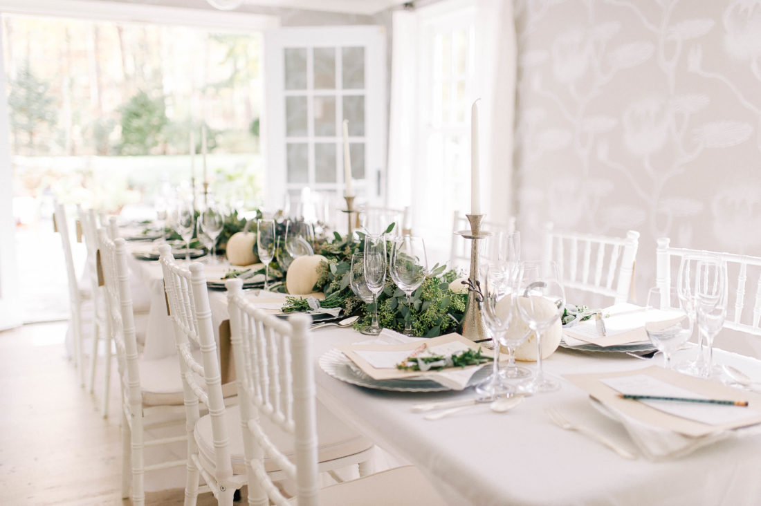 Crisp and modern white, flax, and silver tablescape at Eva Amurri Martino's Friendsgiving, featuring a long eucalyptus garland and white pumpkins