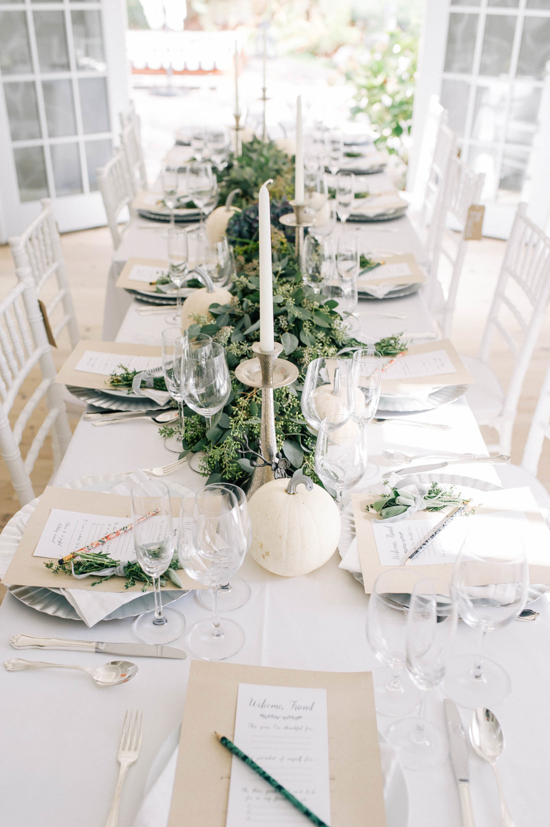 Crisp and modern white, flax, and silver tablescape at Eva Amurri Martino's Friendsgiving, featuring a long eucalyptus garland and white pumpkins