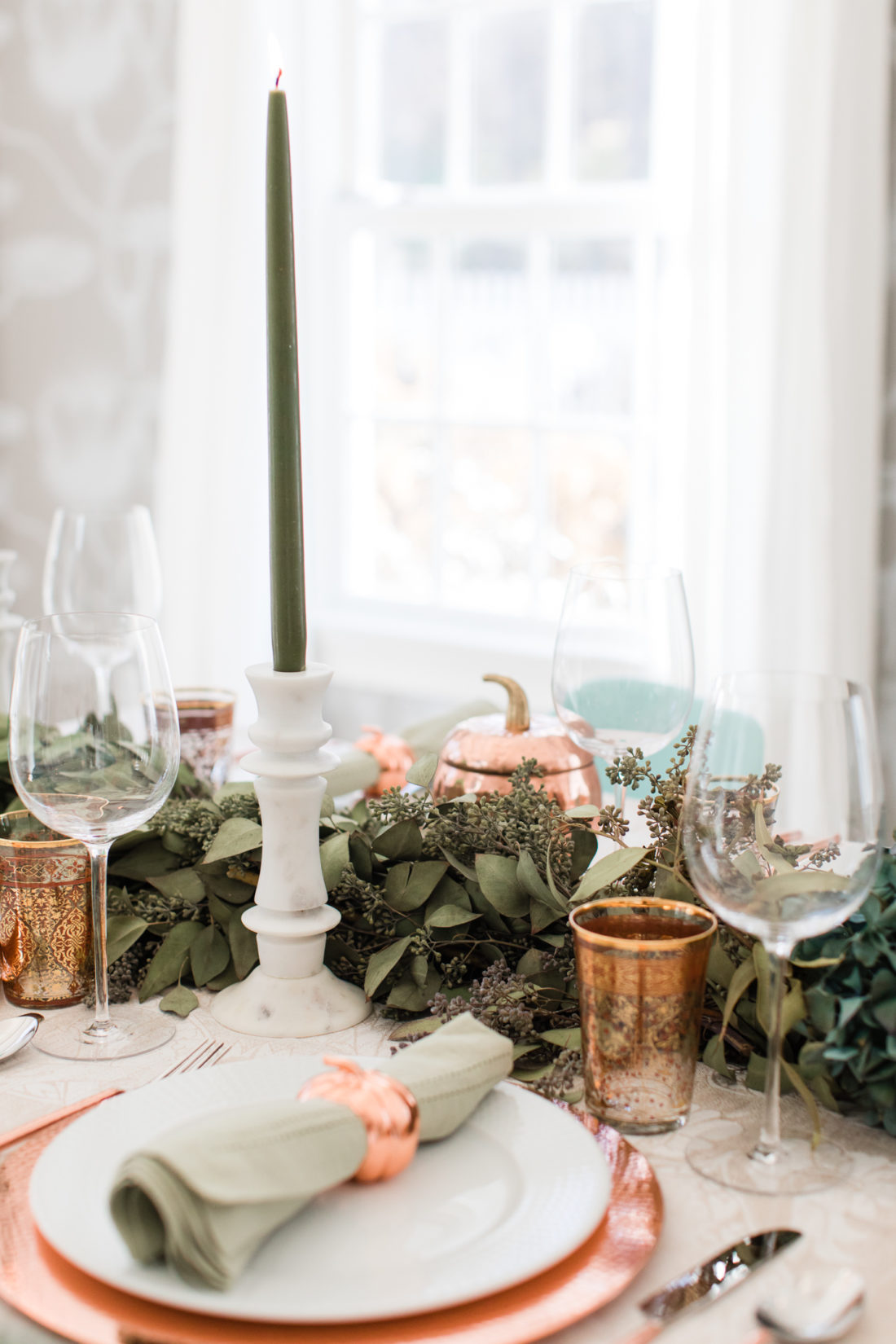 A eucaluptus garland, marble candlesticks with green candles, and a green and copper color scheme add style to Eva Amurri Martino's thanksgiving table