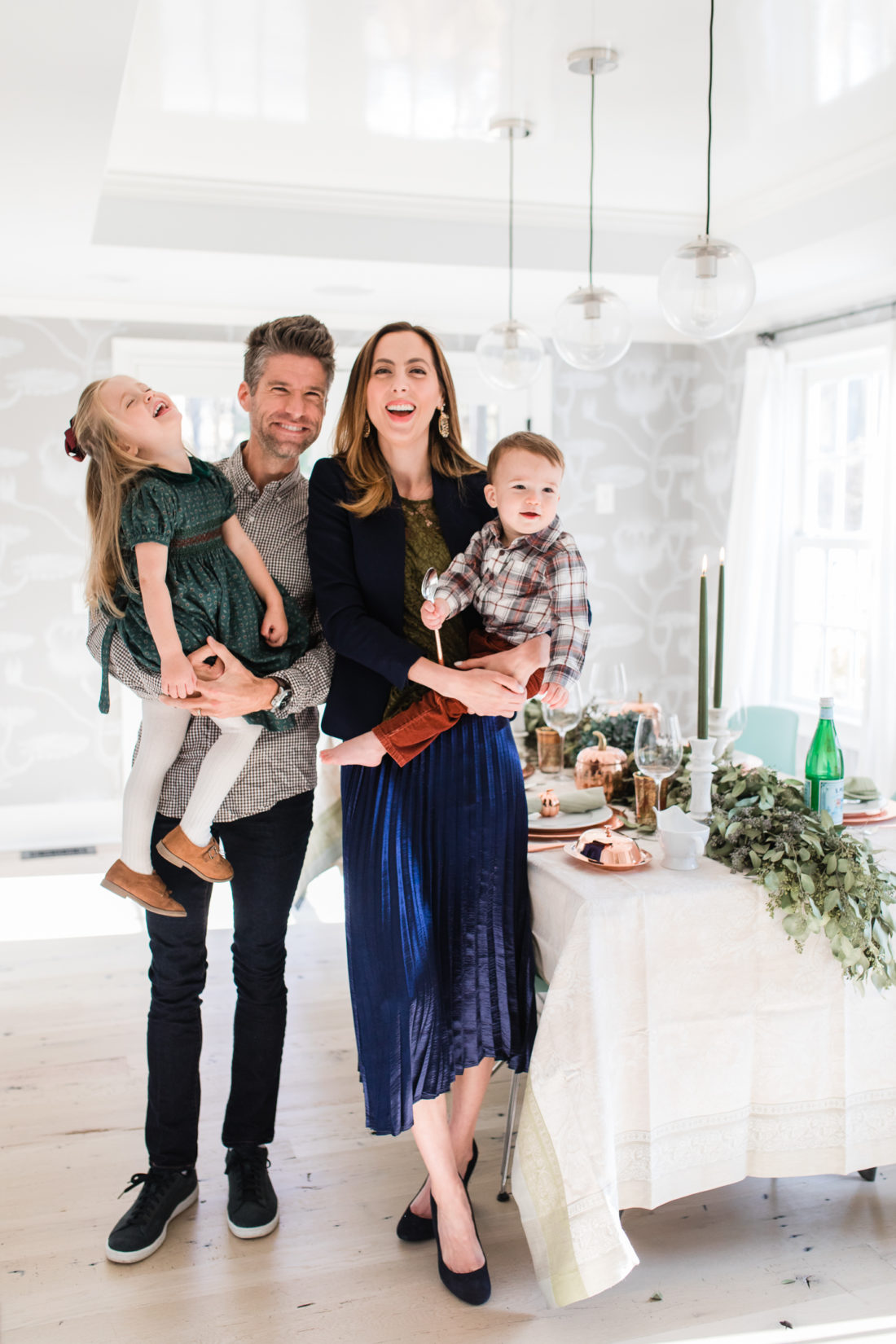 Eva Amurri martino standing with her family, Kyle Martino, Marlowe Martino, and Major Martino, in their dining room set up for Thanksgiving