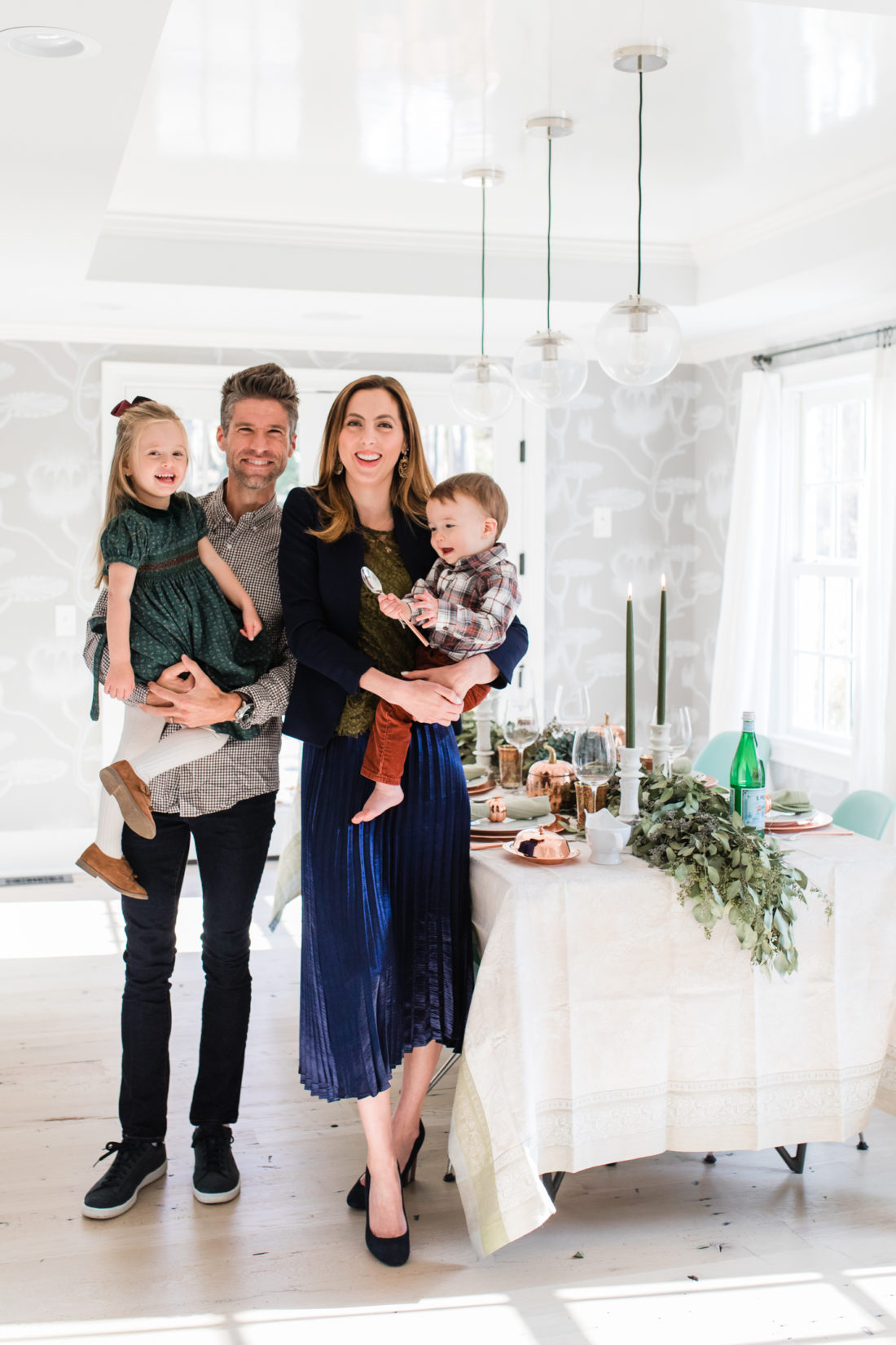 Eva Amurri martino standing with her family, Kyle Martino, Marlowe Martino, and Major Martino, in their dining room set up for Thanksgiving