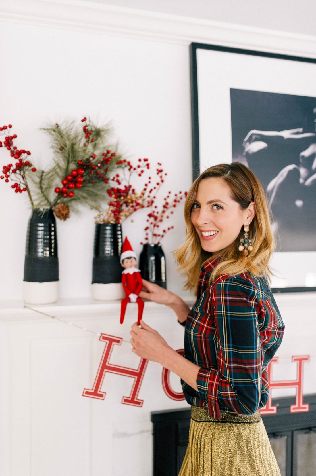 Eva Amurri Martino wears a plaid shirt and puts the Elf On The Shelf on the mantel in her kitchen