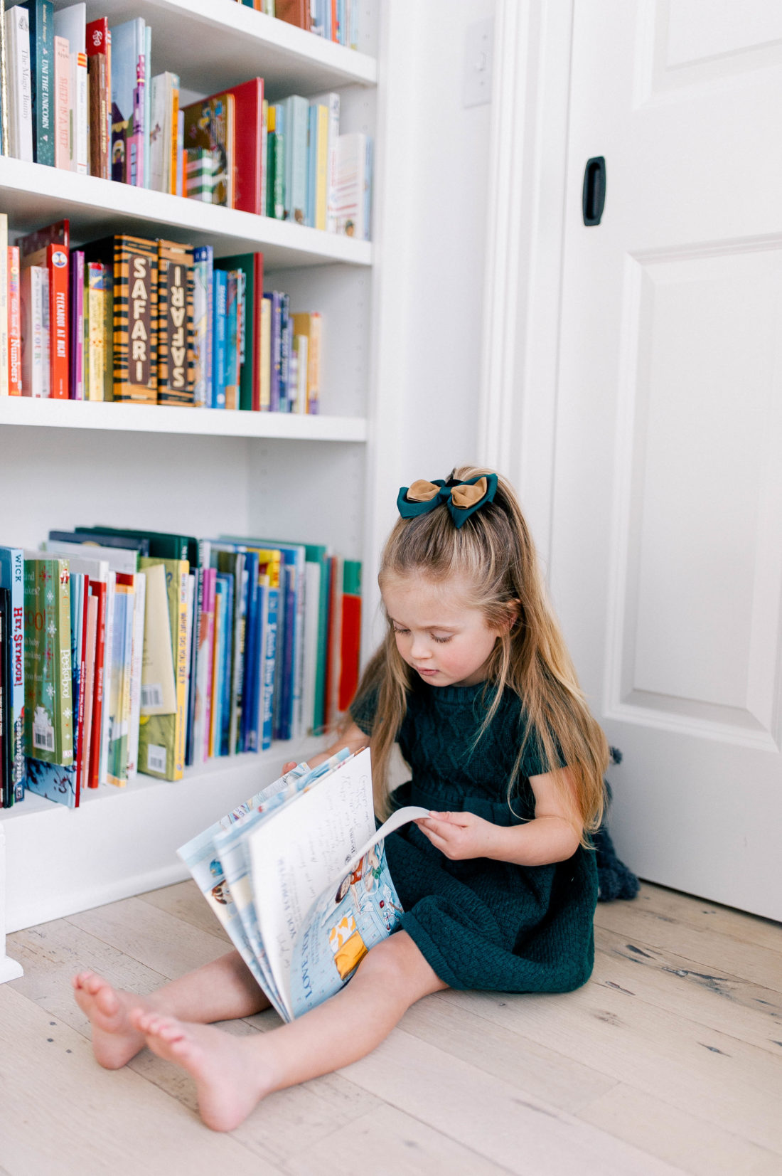 Marlowe Martino wears a hunter green dress and sits on the ground reading books at her home in Connecticut