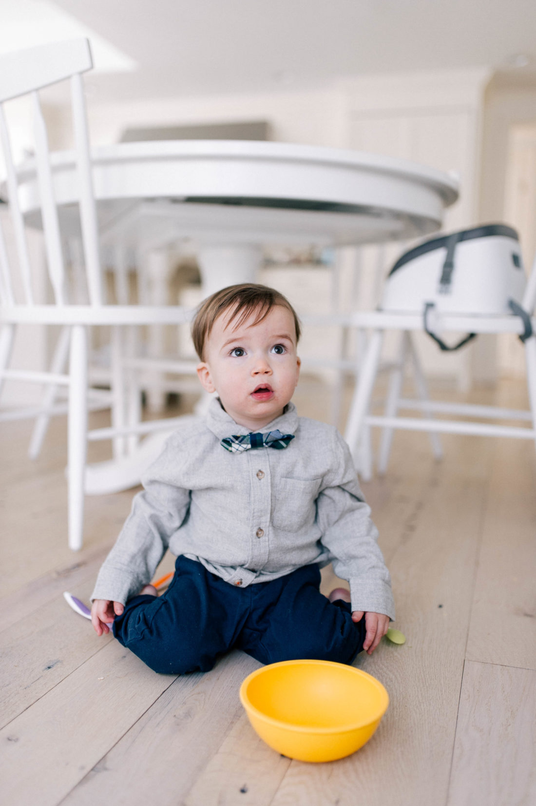 Major Martino wears a grey flannel button down shirt and tartan bow tie, and sits on the kitchen floor in his Connecticut home