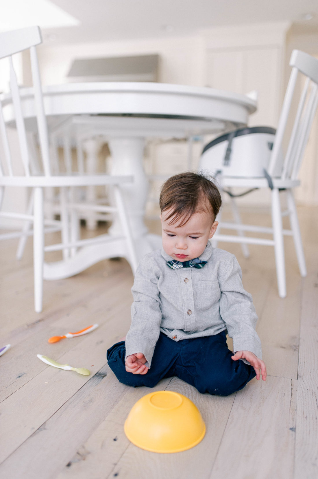 Major Martino wears a grey flannel button down shirt and tartan bow tie, and sits on the kitchen floor in his Connecticut home