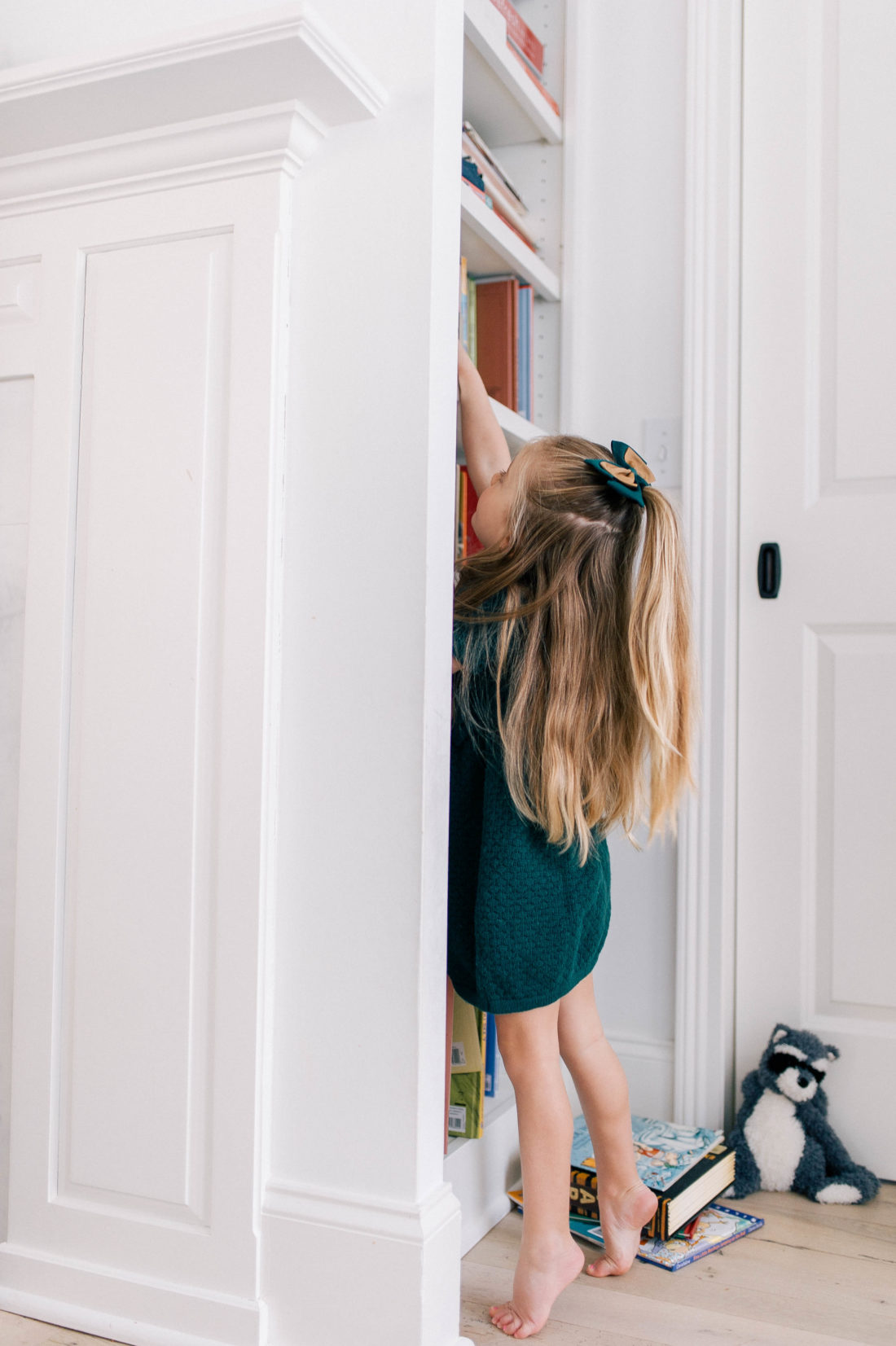 Marlowe Martino wears a hunter green dress and reaches up to pull a book from the book shelf at her home in Connecticut