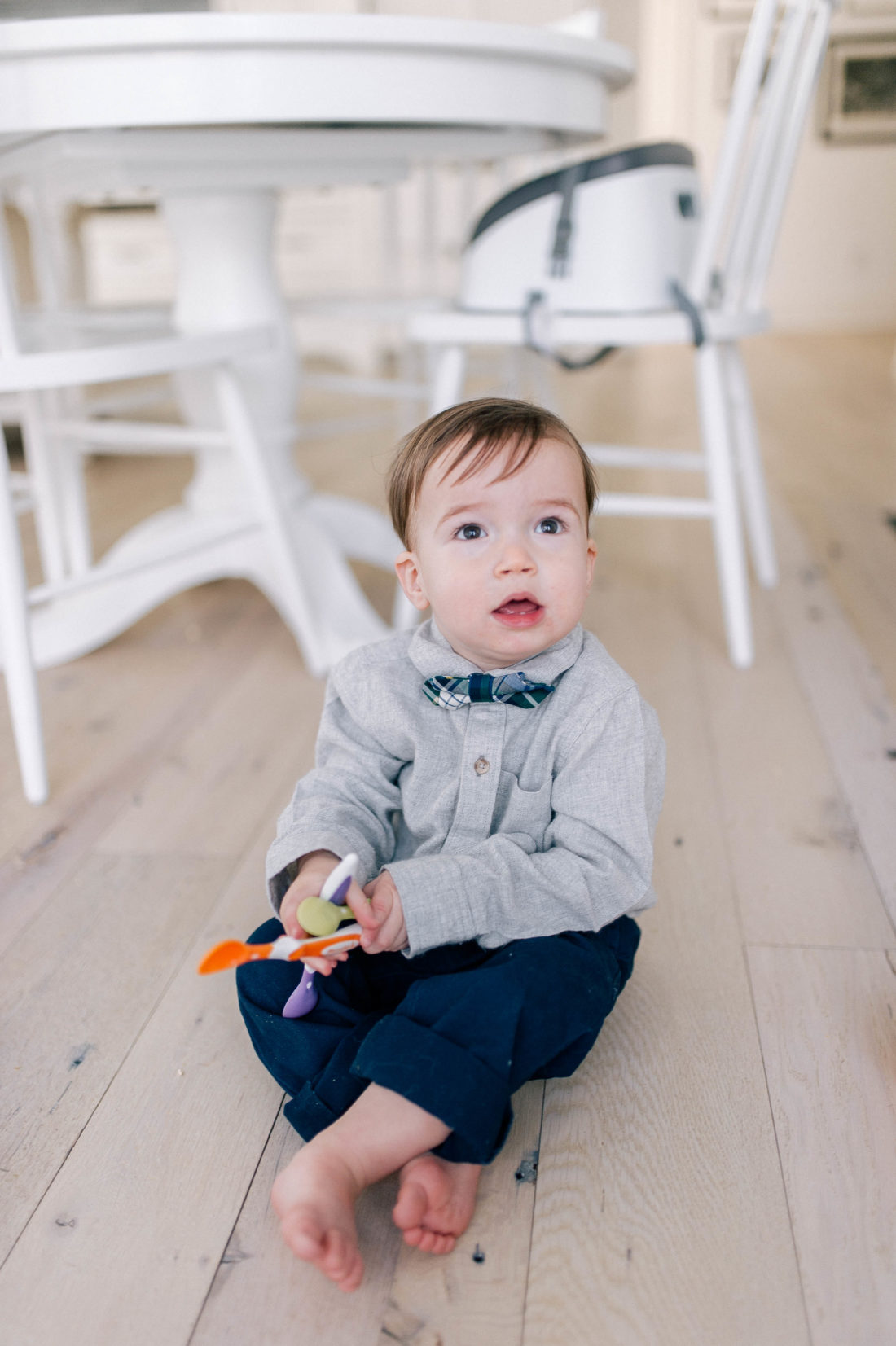 Major Martino wears a grey flannel button down shirt and tartan bow tie, and sits on the kitchen floor in his Connecticut home