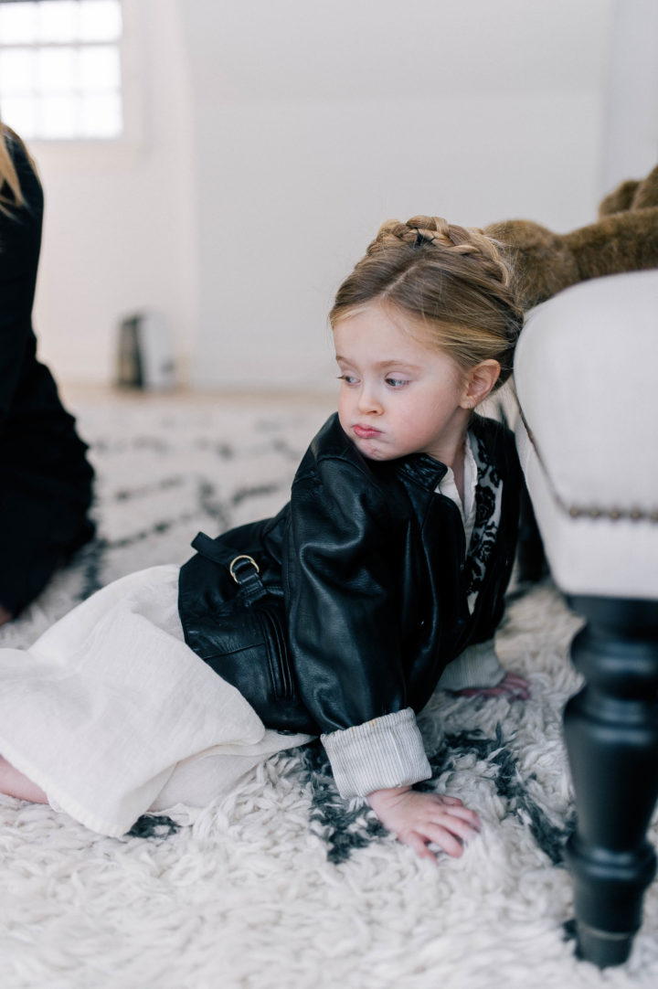 Marlowe Mae Martino makes a pouty face wearing a leather jacket with a halo braid in her hair while lying on the rug in her parents bedroom in Connecticut.