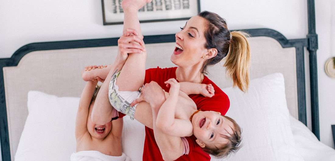 Eva Amurri Martino wears a red sweater and jeans, and lifts one year old son, Major, in the air to tickle him