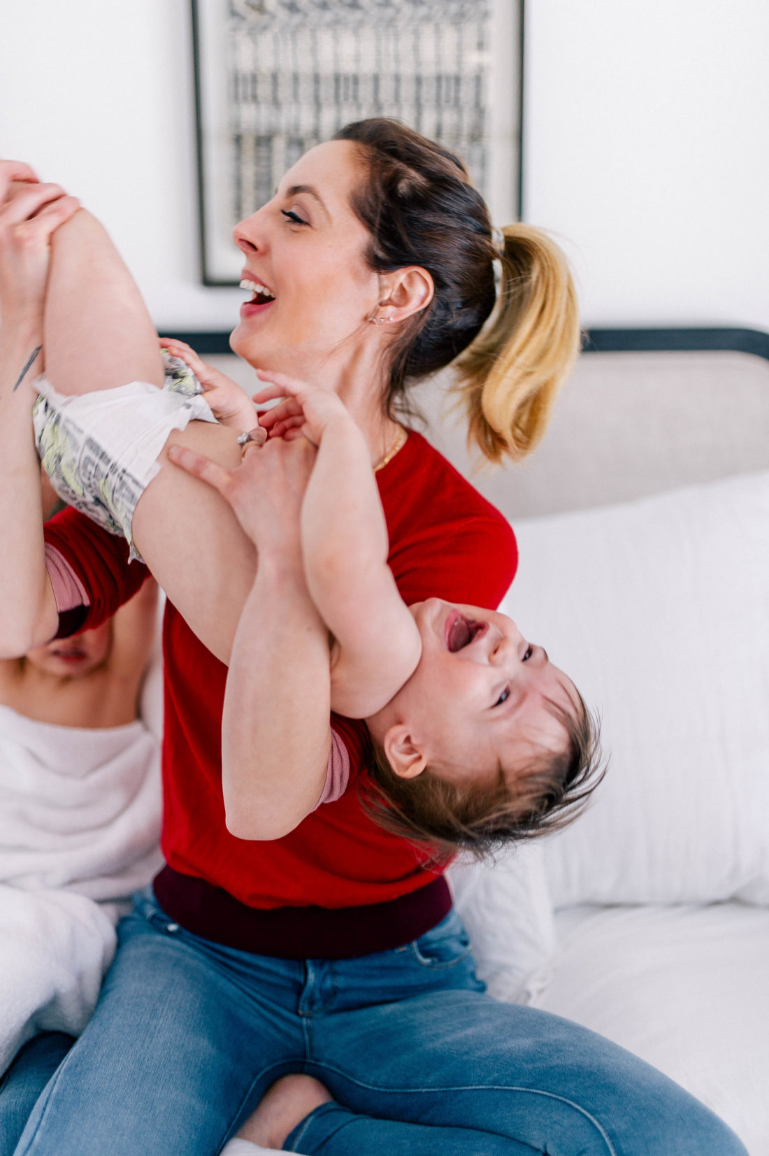 Eva Amurri Martino wears a red sweater and jeans, and lifts one year old son, Major, in the air to tickle him