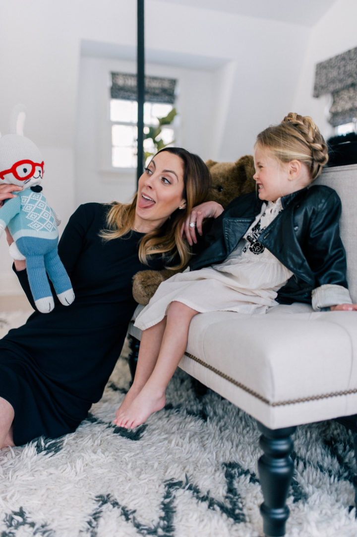 Eva Amurri Martino plays with a doll on the floor with her daughter Marlow Mae Martino who is wearing an ivory tunic dress, leather jacket, and halo braid. 