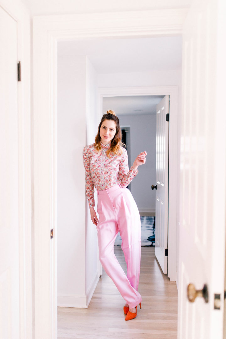 Eva Amurri Martino wears the hottest spring fashion trends: wide pink trousers, a pink floral button up shirt, and her hair in a half up half down topknot in her Connecticut home.