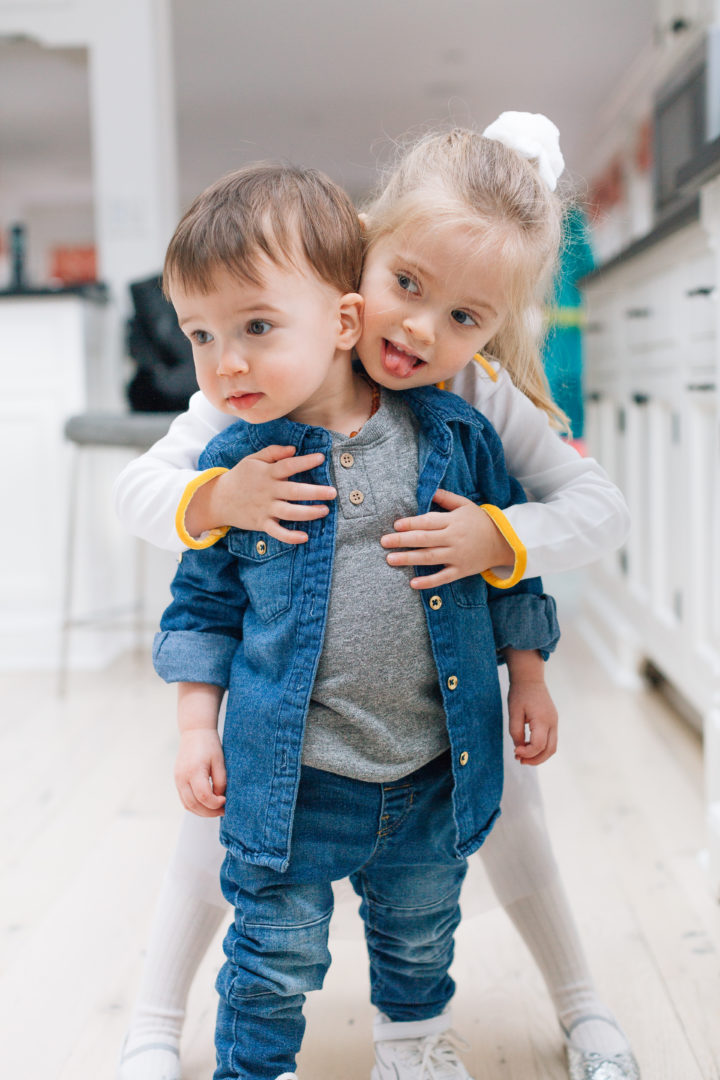 Stylish tot, Major Martino, wears a trendy denim button up over a grey t-shirt, while he gets a hug from older sister Marlowe.