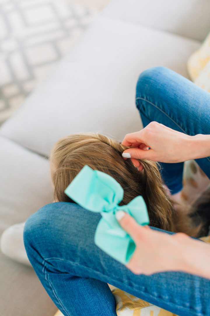 Eva Amurri Martino styles her daughter Marlowe's hair while she sits on the couch with a blue bow hairtie.