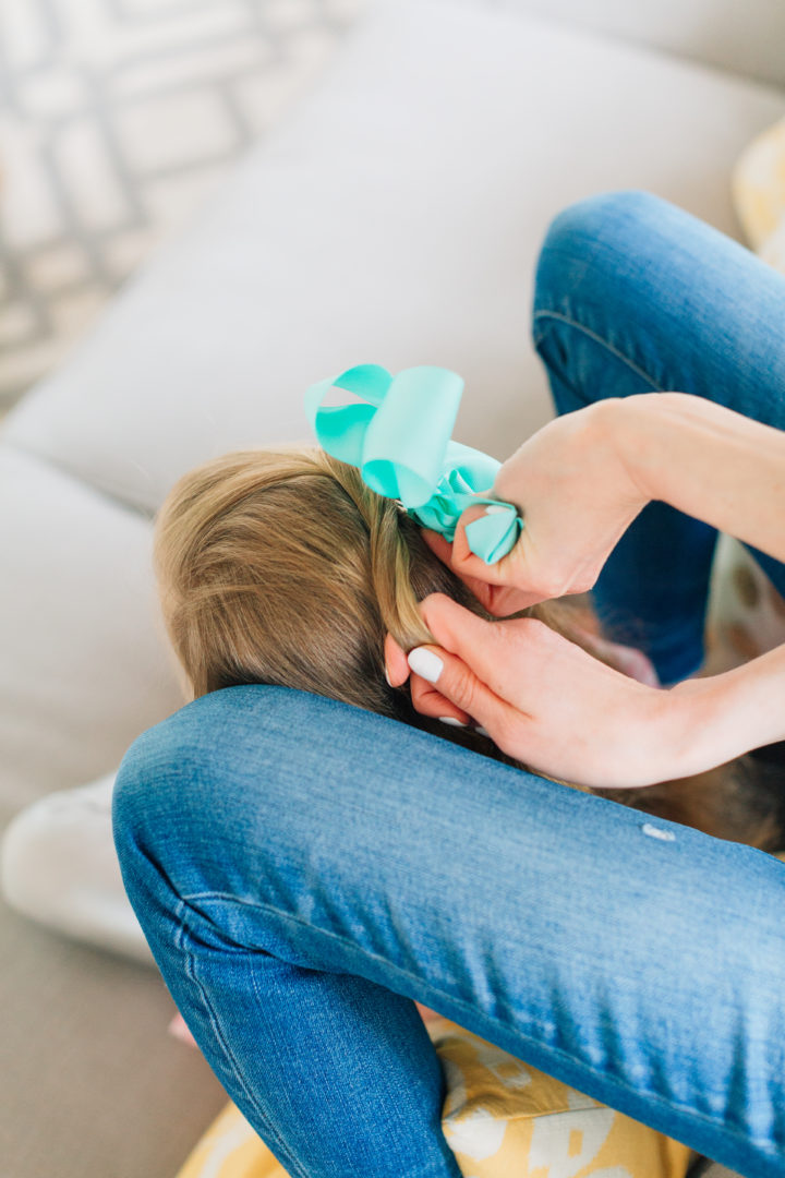 Eva Amurri Martino styles her daughter Marlowe's hair while she sits on the couch with a blue bow hairtie.