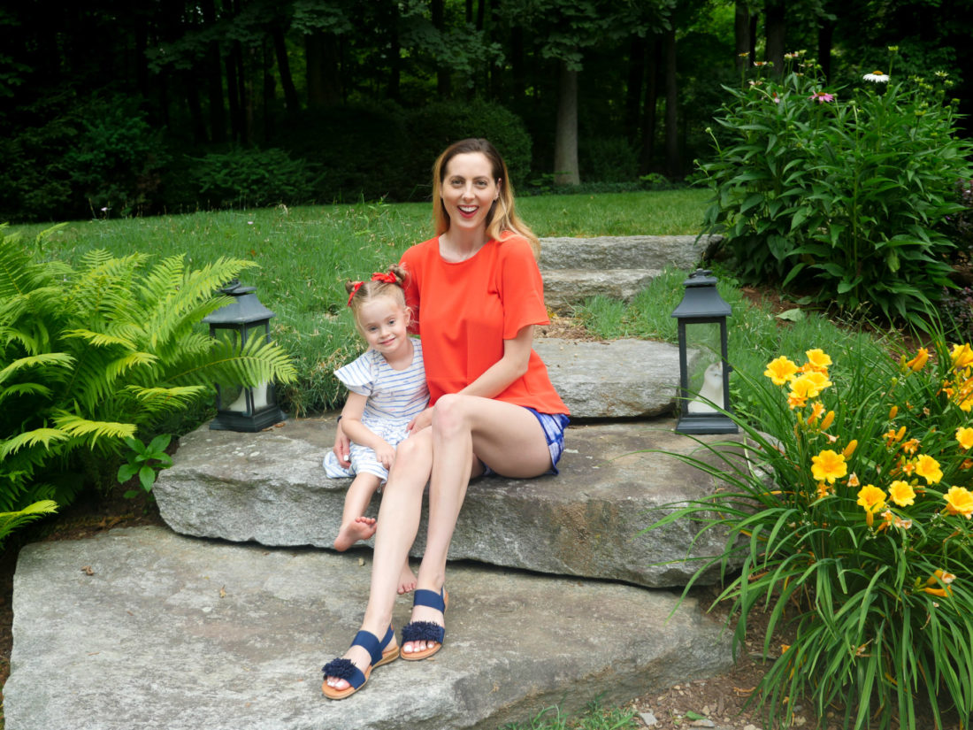 Eva Amurri Martino wears a red top and patterned blue and white shorts, and sits on the steps in her backyard on the fourth of july