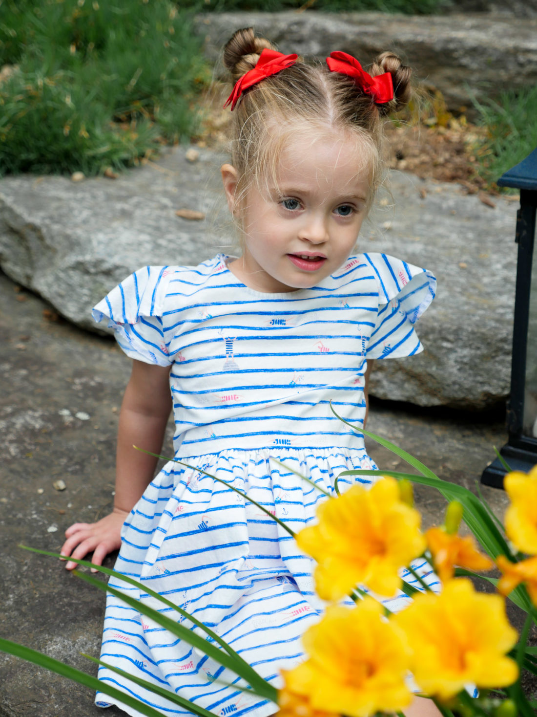 Marlowe Martino sits beside some daffodils wearing a red white and blue dress on the fourth of july