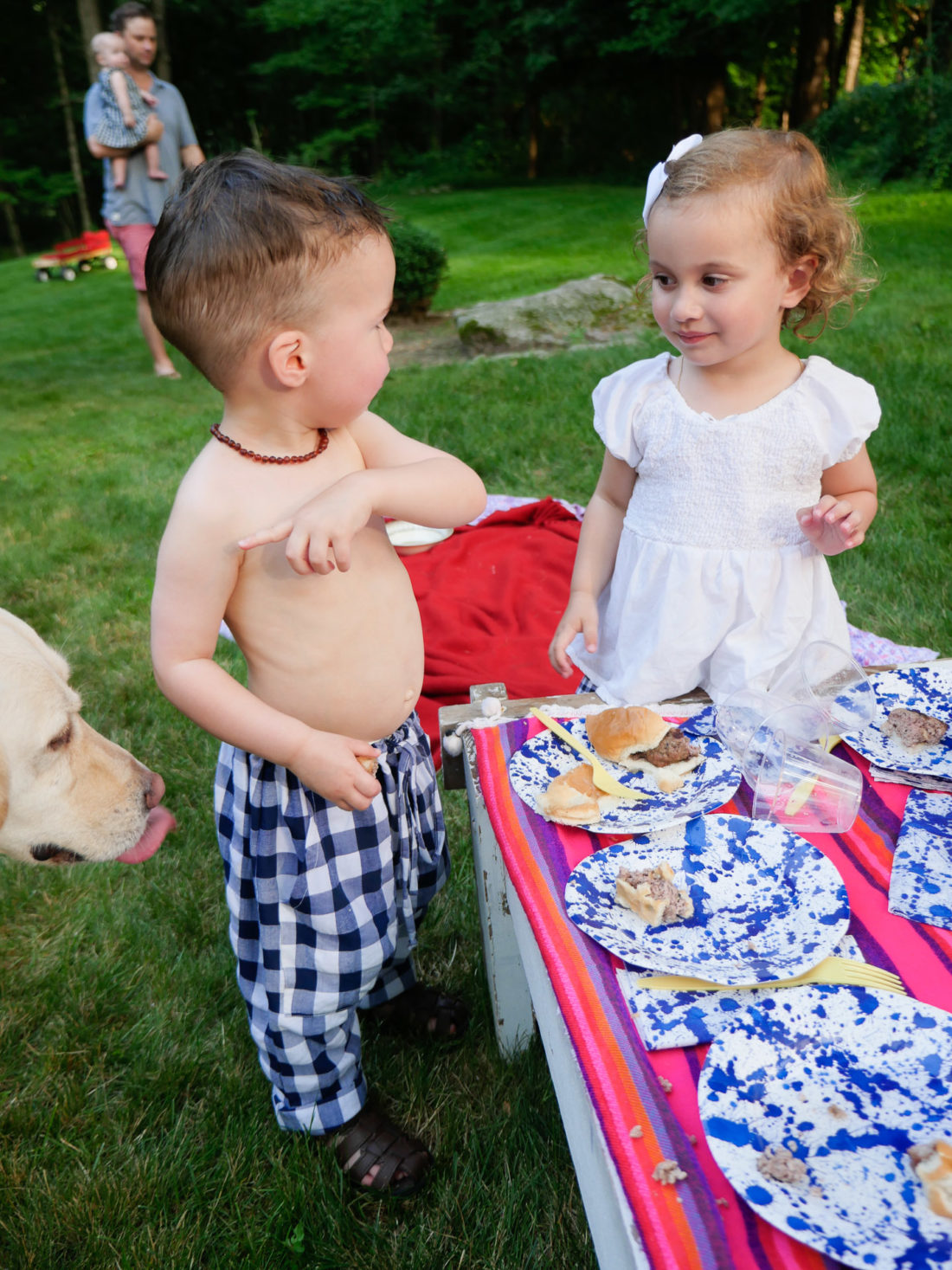 Major Martino wears white and blue checked pants and stands with a little girl on the fourth of july in Connecticut