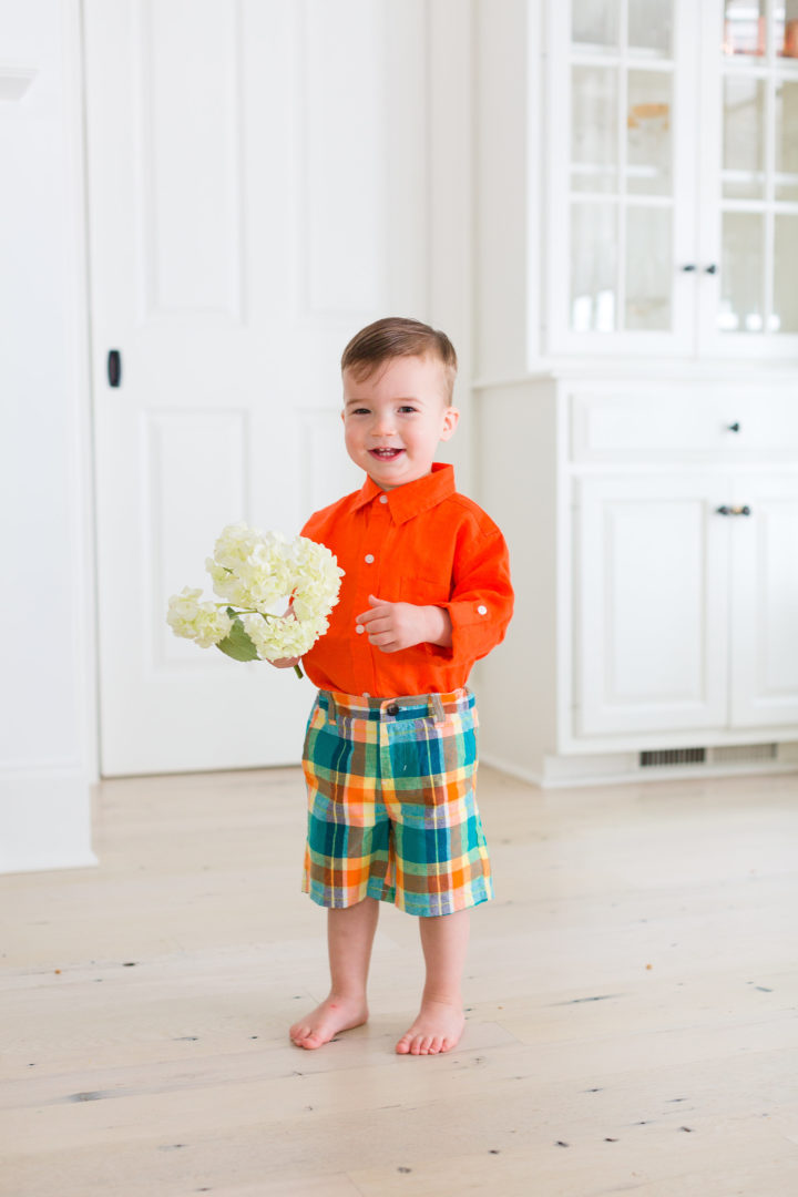 Eva Amurri Martino's son Major wears a pair of colorful green plaid shorts and an orange button up shirt while holding a handful of hydrangeas.