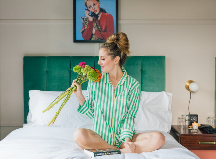 Eva Amurri Martino sits on a bed in a pair of green striped JCrew pajamas holding a bouquet of flowers