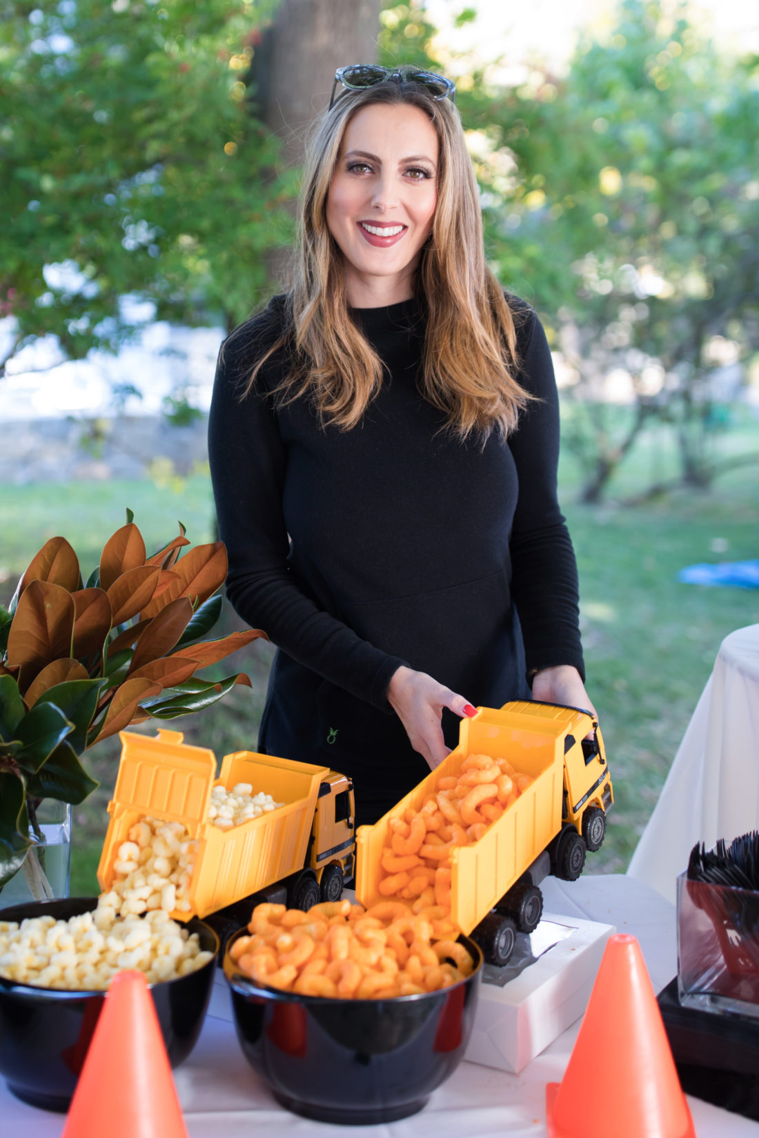 Eva Amurri Martino stands in front of a table full of snacks cleverly served inside of tractors to match the Construction Theme of her son Major's 3rd Birthday party
